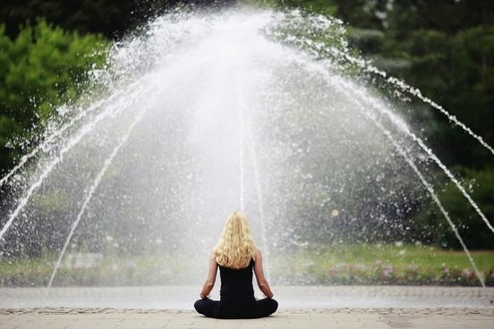 Frau im Yogasitz vor einem Springbrunnen